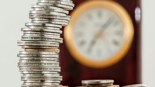 A close-up image of stacked coins with a blurred clock, symbolizing time and money relationship.